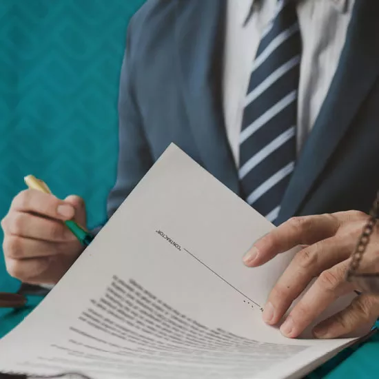 A man wearing a suit writes on a set of legal documents.