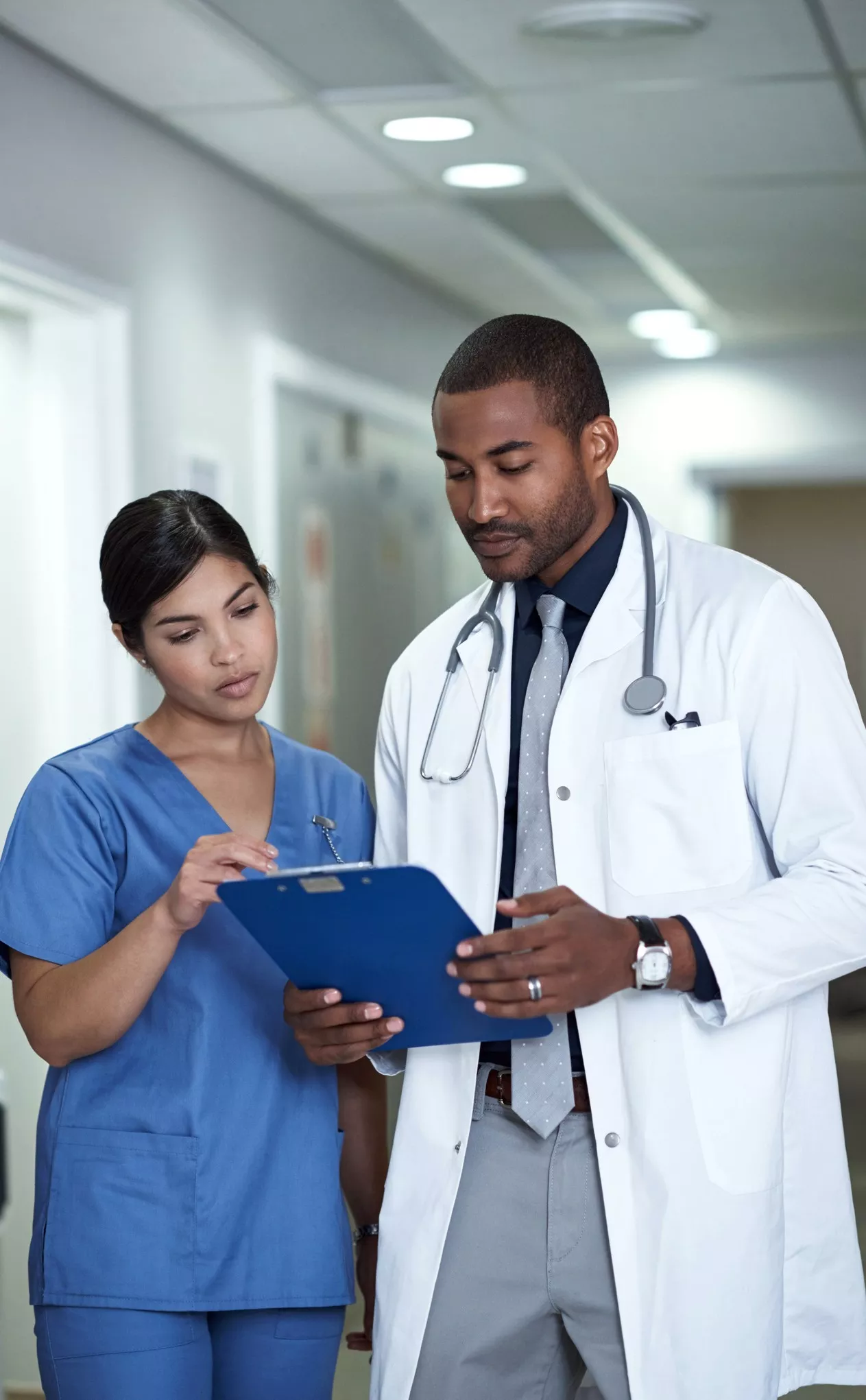 Shot of two doctors discussing a medical record together while standing in a hospital corridor